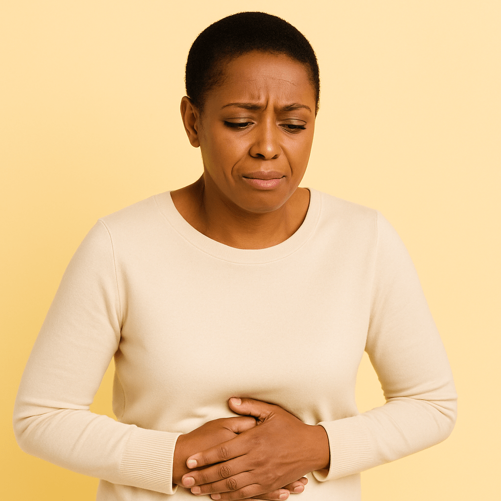 Black woman in her 40s with short natural hair holding her stomach and looking mildly uncomfortable against a soft butter-yellow background, illustrating how abdominal discomfort can appear during menopause.