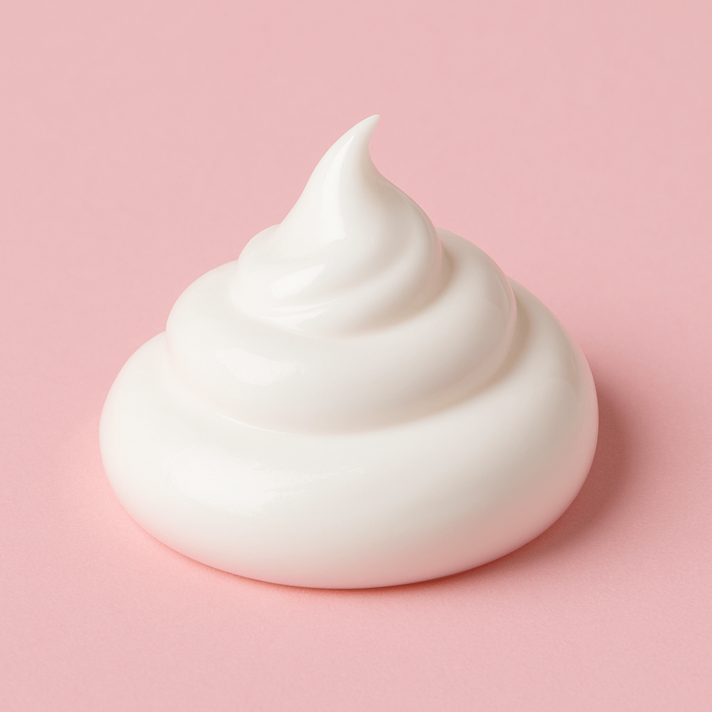 Close-up of a smooth, glossy swirl of white face cream on a rose-pink background, representing topical estrogen creams like estradiol and estriol used to support menopausal skin health.